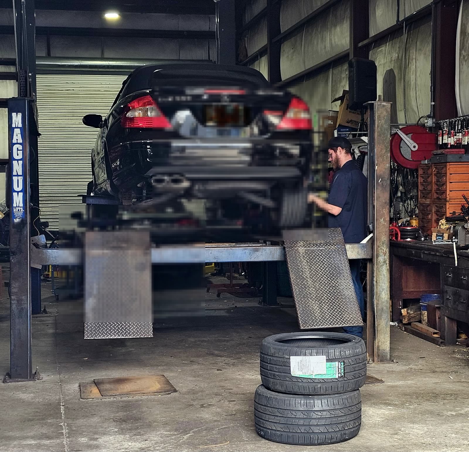 Mechanic working on a car raised on a Magnum lift, new tires in the foreground